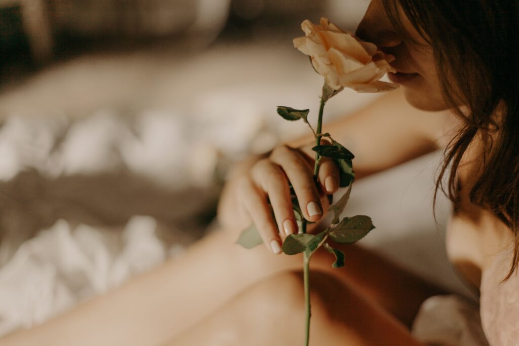 A serene close-up of a woman gently holding and smelling a rose in soft lighting.